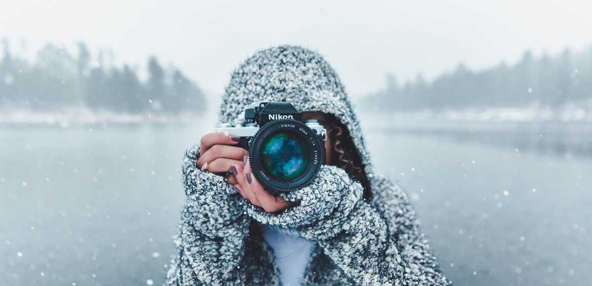 Symbolbild: Eine Frau macht ein Foto vom Fotografen vor einem See im Schnee