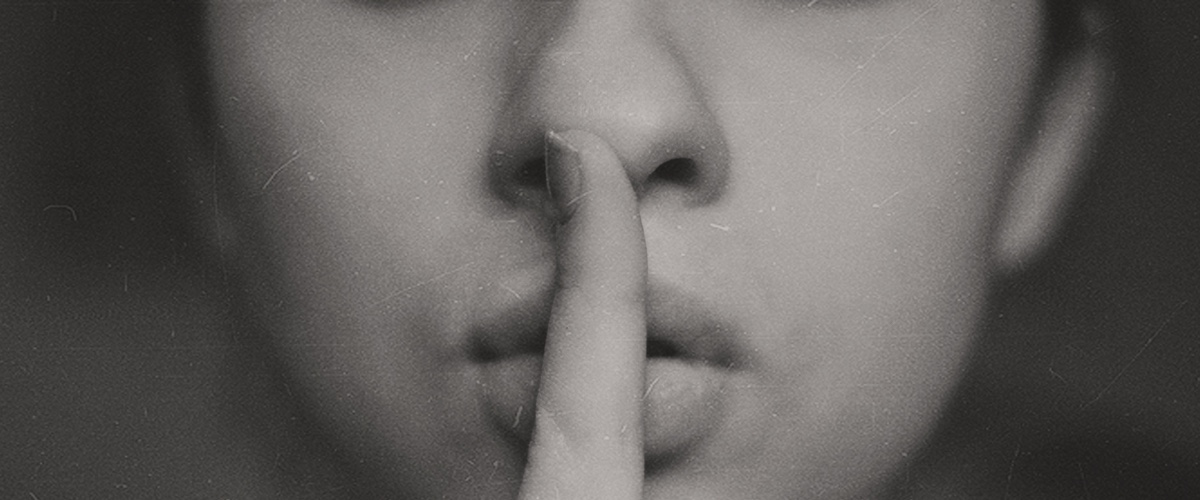 Symbolbild: Ein schwarz-weiß Bild einer Frau, die ihren Zeigefinger vor den Lippen hält