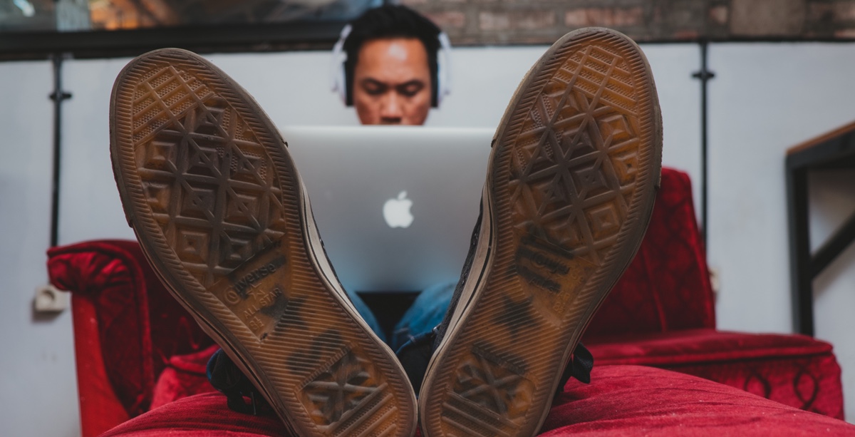 Symbolbild: Ein Mann sitzt mit den Füßen auf einem Sofa und arbeitet an einem Notebook