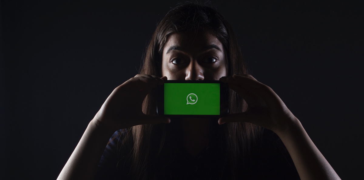 messenger_unternehmen Symbolbild: eine Frau hält sich ein Smartphone mit dem WhatsApp-Logo vors Gesicht